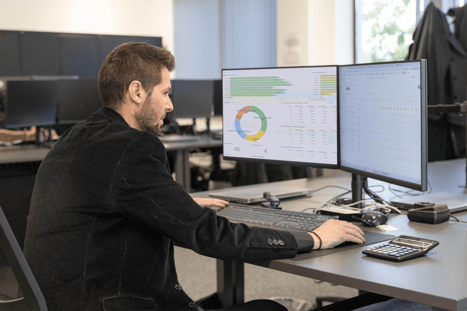 A bodyshop manager sitting in the office of a repair shop, tracking live business performance data and employee productivity insights through the intuitive bodyshop management system, Onyx BMS.